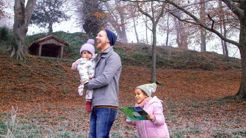 ather holding a baby laughs while walking beside a small child holding a map. In the background, frost and winter trees cover the Weir Garden.